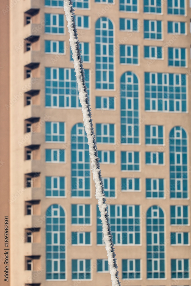 Fototapeta premium A wire frozen by snow and ice against a backdrop of a multi-story building