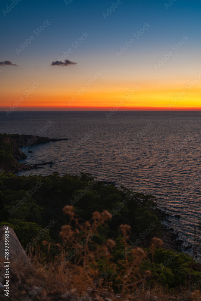Fototapeta premium Colorful sunset over calm sea and rocky coastline landscape