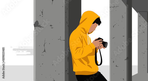 A focused individual in a vibrant yellow hoodie stands between concrete pillars, meticulously operating a camera, embodying urban photography and creative art.