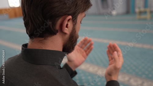 Muslim male making Dua and praying in a mosque with a rosary. Young Muslim man supplicating during Ramadan at masjid. Spiritual Islamic worship and devotion concept with a Sheikh.