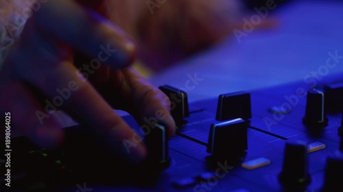 Man DJ playing music on electronic mixer controller at disco club. Male disk jockey mixing sound on set in night club. Hand of guy on turntable panel. Close up. Clubbing vibe, neon party, mix console