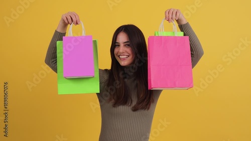 Cheerful girl joyfully showing off her colorful shopping bags while smiling widely at the camera in a playful moment, radiating happiness and excitement during her shopping experience.