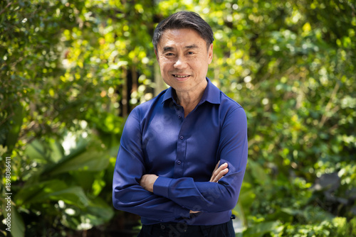 Happy smiling Asian senior man with grey hair, showing positive confident expression in arm crossing gesture, real people model