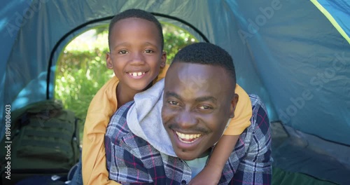 African American father and child piggyback playing after child opening eyes in tent with backpack