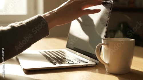 Person typing on laptop next to coffee mug in warm sunlight.