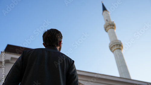 Canvastavla Young Muslim man looking at a tall mosque minaret under blue sky