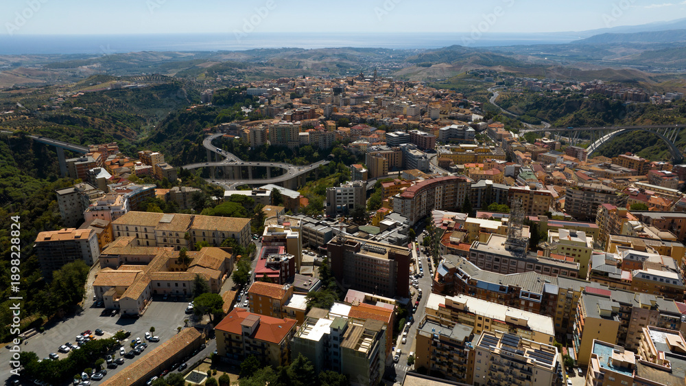 Fototapeta premium Panoramic aerial view of the city of Catanzaro, capital of the Calabria region in southern Italy. In the foreground are the town's houses, buildings, and rooftops. The Ionian Sea is on the horizon.
