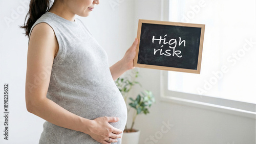 Pregnant woman holding chalkboard with high risk text, maternity health awareness, expecting mother with potential complications in bright room, healthcare pregnancy concept