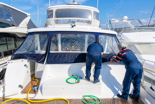 Quadro su tela Two workers performing maintenance on the bow of a yacht at a marina, leaning ov
