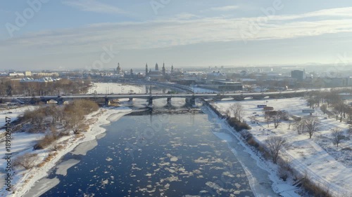 Wallpaper Mural Dresden Elbe panorama in winter: Ice floes drift on the river in front of the historic old town skyline. The riverbanks are deeply covered in snow under a vast, bright sky. Torontodigital.ca
