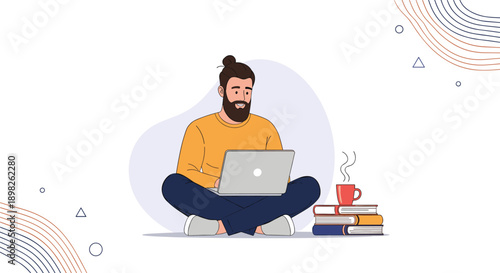 Young bearded man with a man bun sitting on the floor with a laptop studying or working remotely with coffee and books nearby.