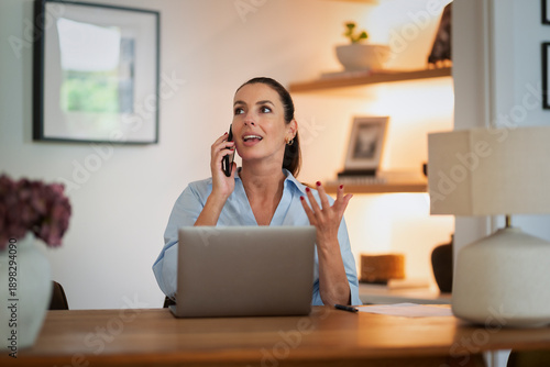 Confident woman sitting at table, using computer and holding a cell phone in his hand and talking on the phone