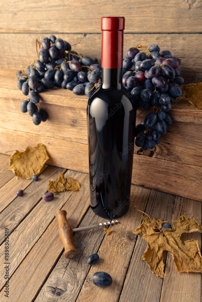 Fototapeta premium Bottle of red wine with blue grapes on a wooden table.