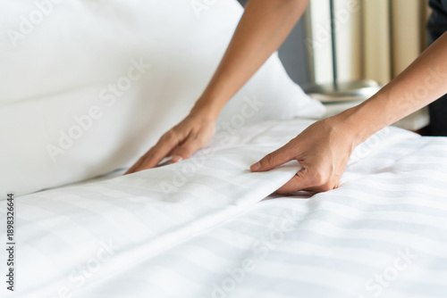 Close up of a housekeeper woman making a bed in a hotel bedroom. Room service, housework concept