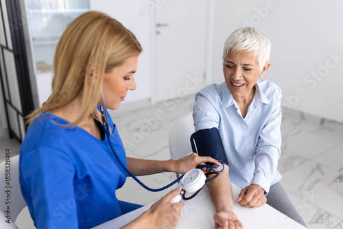 Medical checkup for senior. Smiling elderly woman getting blood pressure measured by female nurse in clinic. Healthcare and medicine concept, doctor using stethoscope and monitor for diagnostic.
