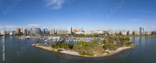 Aerial view of a vibrant cityscape meeting the serene harbor dotted with yachts, lush green park, and sandy beach, Sarasota, Florida, United States.