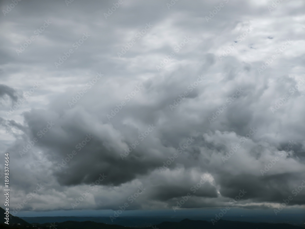 Obraz premium Dense grey storm clouds swirl across a dark, moody sky over a faint mountain horizon. This dramatic atmospheric scene captures the raw power of nature before a heavy rain in the highlands.
