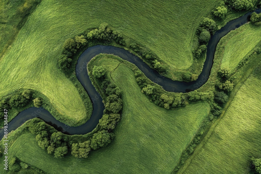 Fototapeta premium Winding river flows through vibrant green hills, showcasing natu