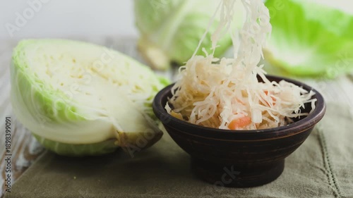 A rustic clay bowl with homemade fermented cabbage on a wooden table.