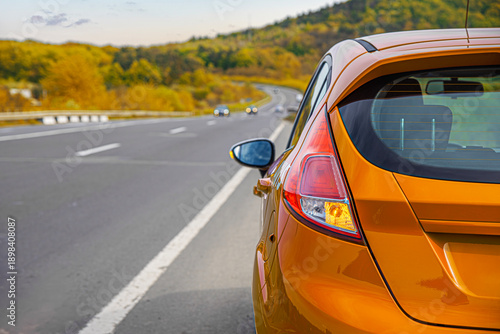 Foto A vibrant orange hatchback is parked on the shoulder of a scenic highway that winds through autumn-colored hills