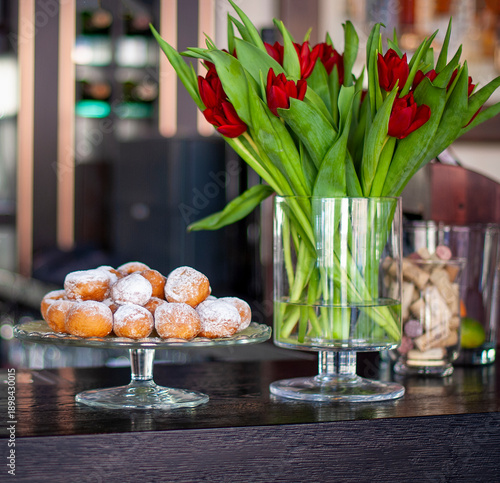 Many donuts on a glass tray with tulips flowers in a vase