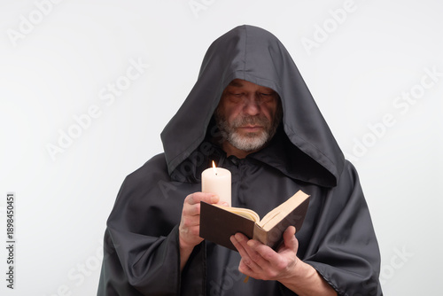 Photos Bearded monk in hood holding candle and reading text.