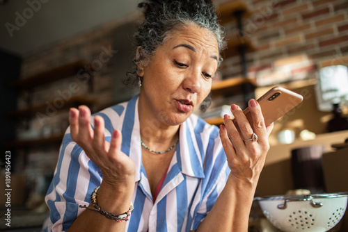 Mature woman frustrated with smartphone in home kitchen