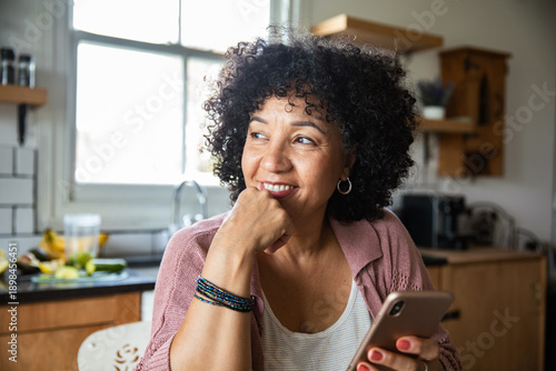 Smiling middle-aged woman with smartphone at home kitchen
