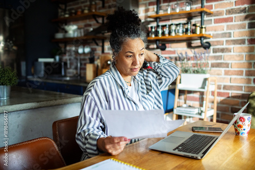 Mature woman reviewing bills at home kitchen table