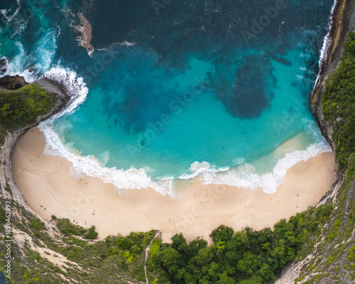 Aerial view of Kelingking Beach's dramatic cliffs plunging into the turquoise sea, with white sand meeting the foamy waves, Klungkung Regency, Bali, Indonesia.