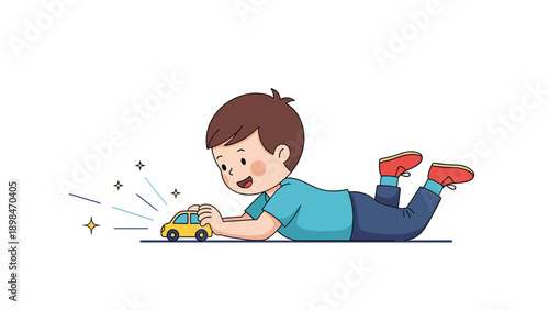Happy young boy lies on his stomach on the floor and plays with a small yellow toy car that has sparkling details.