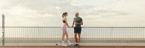 Wallpaper Mural Male and female athletes are talking outdoors on the seafront, walking bridge. Happy fit people are cheerfully talking while working out. Minimalism sport aesthetic. Panoramic Torontodigital.ca