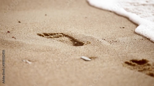 Woman footprint fading in sandy beach as gentle wave washes away marks