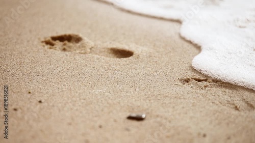 Woman footprint on sandy beach being gently erased by advancing ocean waves during daylight