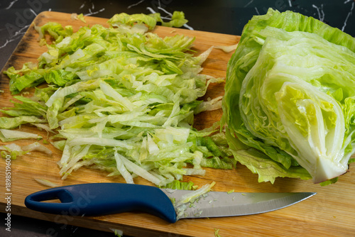 Cuadro en lienzo a wooden cutting board featuring a pile of shredded green lettuce next to a partially sliced head of iceberg lettuce and a knife with a blue handle