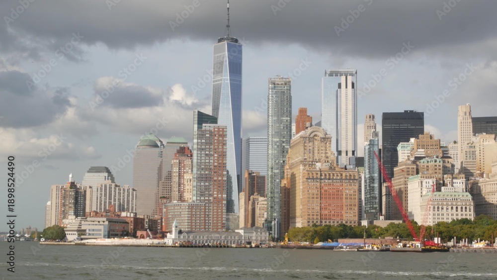 Obraz premium New York City Manhattan Downtown skyline from ferry boat to Liberty Island, United States. Financial District cityscape, World Trade Center skyscraper tower. Urban buildings architecture. Rain clouds.