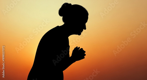 Woman in silhouette praying with hands clasped at sunset with orange and yellow gradient background