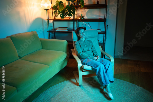 Fotografija Loneliness and depression of elder people, senior woman sat in chair at home in rgb light looking with apathy and sadness, life crossroads drama and mental exhaustion caused by drama in relationships