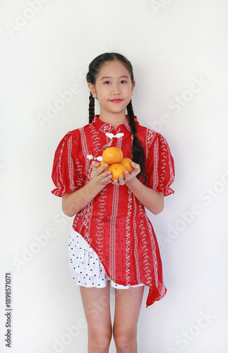 Asian girl in stylish red Chinese-inspired outfit, smiling gracefully while holding handful of fresh oranges to symbolize prosperity and luck for the Lunar New Year celebration.