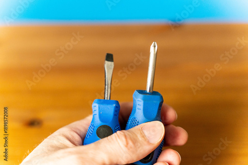 Fotografija Hand holding two screwdrivers with blue rubber grips, one flathead and one Phill
