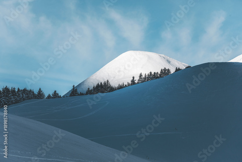 snow covered mountain near col de lautaret in french alps with illuminated height and pine forest