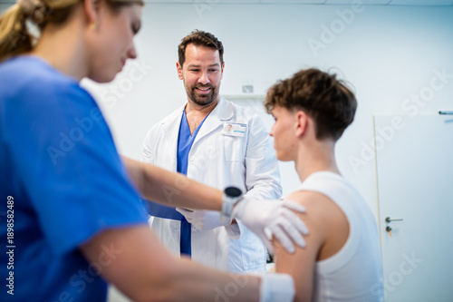 фотографія Doctor giving flu vaccine to teenage boy in medical clinic.