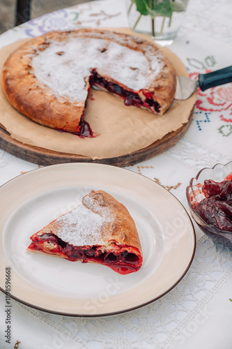 Homemade cherry pie slice served on a table with fresh strawberries, fruit preserves and tea, styled as cozy dessert still life.