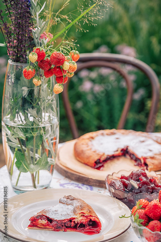 Homemade cherry pie slice served on a table with fresh strawberries, fruit preserves and tea, styled as cozy dessert still life.