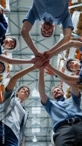 Team of warehouse workers collaborating by stacking hands together, fostering teamwork and camaraderie in a vibrant industrial setting