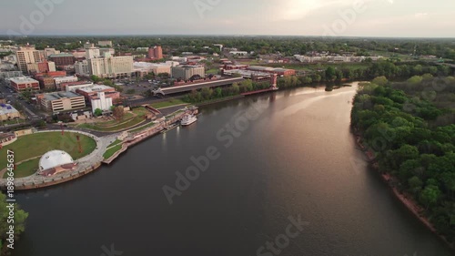 Aerial drone landscape view of downtown Montgomery, Alabama riverfront water park along gun island shoot river with baseball ballpark stadium, green lawn, buildings, high-rises, and capital city roads