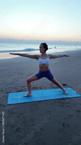 Young lesbian woman practicing yoga warrior pose on the beach