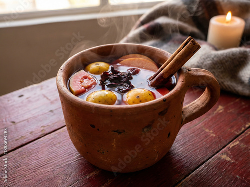 Traditional Mexican Christmas fruit punch in clay mug with steam and cinnamon sticks on rustic wood