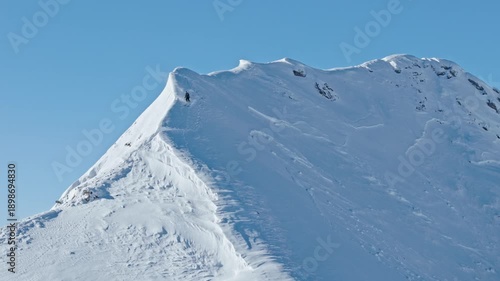 Slow motion aerial footage of a free ride skier carving through fresh powder snow on a steep alpine slope. Dynamic drone shot capturing the thrill of first tracks in pristine winter mountains.