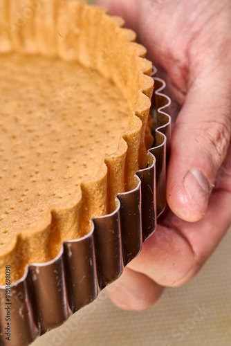 Fotografie Baked shortcrust tart shell in metal ring held by hand